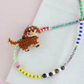 Beaded necklace with a DOG charm on a light pink background