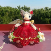 Handmade Cat toy figure in a red dress with floral details on a red surface with greenery in the background