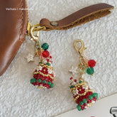 Handmade Christmas tree keychains with red, green, and gold colors on a textured white background.