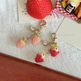 Strawberry-shaped keychains with gold accents on a textured surface.