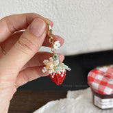 Hand holding a strawberry-shaped keychain with pearl details against a neutral background