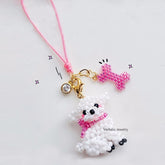 White beaded Bichon frise charm with pink accents on a pink string against a white background, featuring 'Verhalo Jewelry' branding.