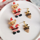 Beaded christmas bear and pinecone earrings on a white plate.