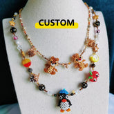 Colorful beaded necklace with animal figures on a mannequin bust, labeled 'CUSTOM'.