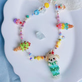 Colorful beaded necklace with a dog pendant and dessert charms on a white plate.