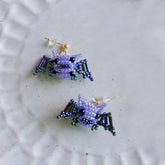 Pair of beaded spider earrings on a textured white surface - Verhalo custom jewely