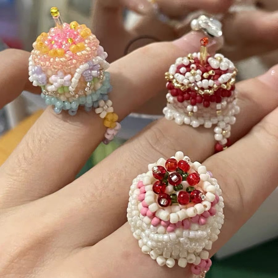 Colorful beaded rings shaped like small cakes held between fingers.