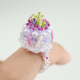 Colorful beaded cake ring on a hand against a white background