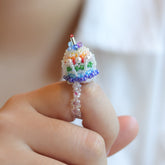 Colorful beaded rainbow cake ring held between fingers against a blurred background