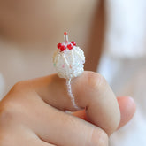 Close-up of a hand wearing a beaded cake ring with red accents on a blurred background