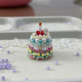 Small beaded cake ring with a candle on a white surface with beads scattered around.