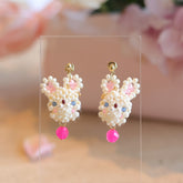 Pair of beaded earrings shaped like bummy with pink accents on a clear stand.