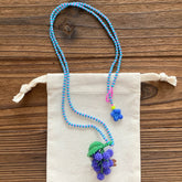 Beaded necklace with a grape pendant on a wooden surface