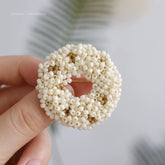 Handmade beaded circular accessory held by a hand against a blurred background