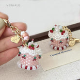 birthday cake bag charm with beaded design and gold heart charm held by a hand on a light background.