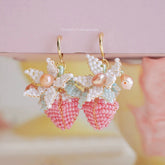 Delicate strawberry-shaped earrings with pearl details on a soft pink background
