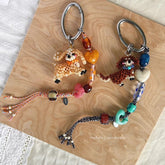 Two dog-shaped keychains with colorful beads on a wooden surface, featuring the brand 'Verhalo Handmade'.