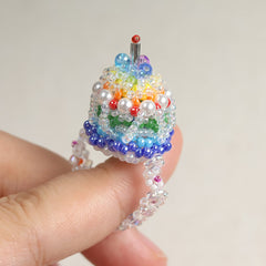 Colorful beaded cake ring held by a hand against a plain background