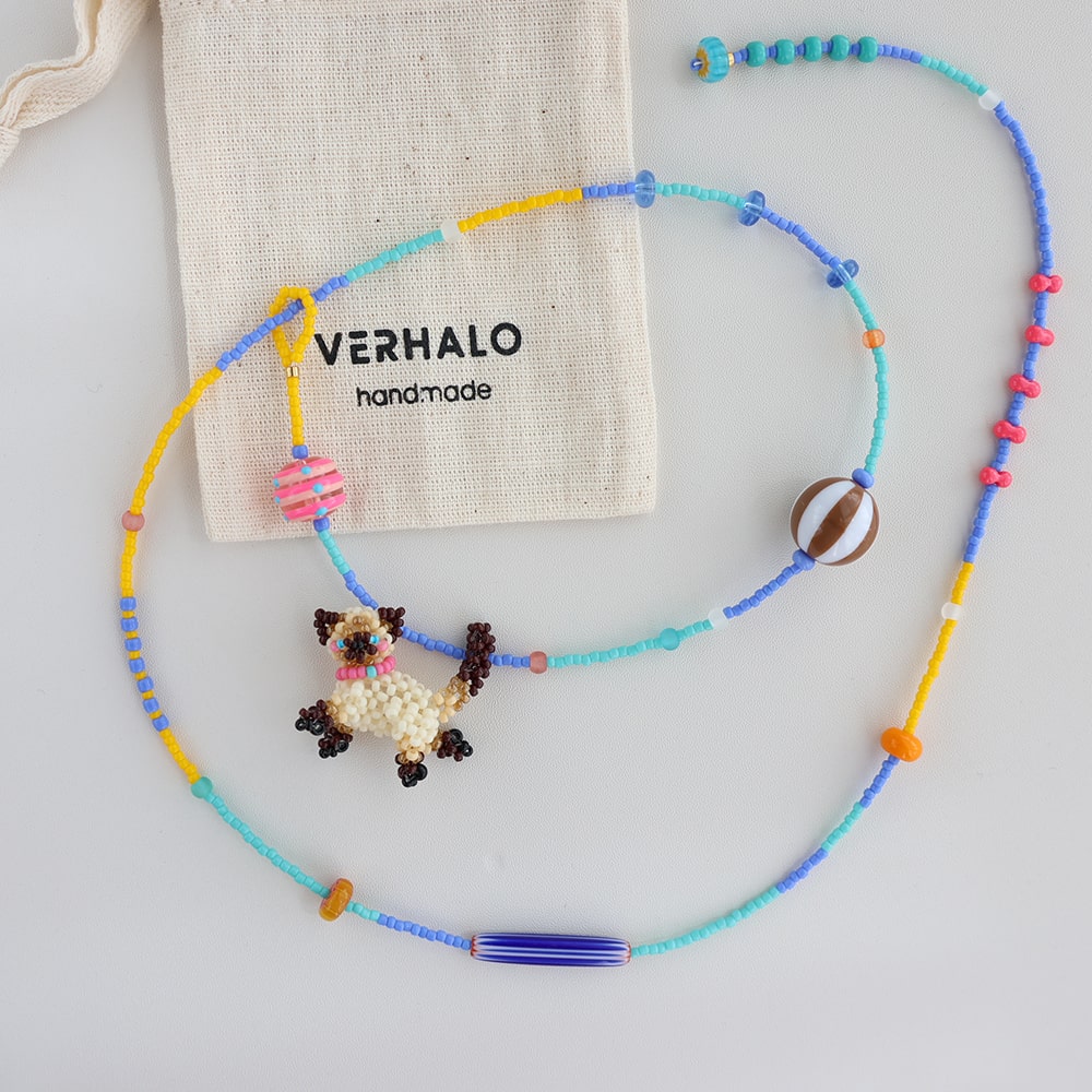 Colorful beaded necklace with a cat charm on a light gray background, featuring a Verhalo branded bag.