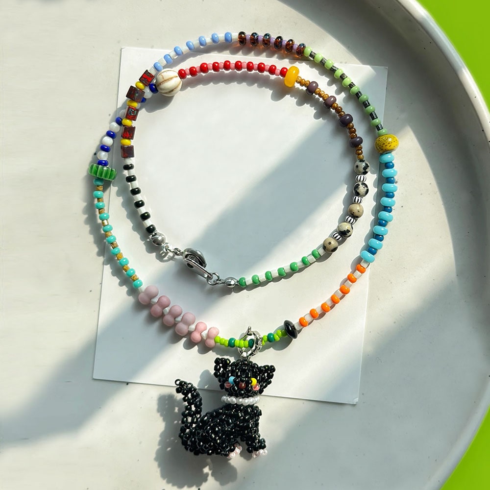 Colorful beaded necklace with a black cat pendant on a white surface - Verhalo Handmade Jewelry