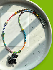 Colorful beaded necklace with a black cat pendant on a white plate. - Verhalo Handmade Jewelry