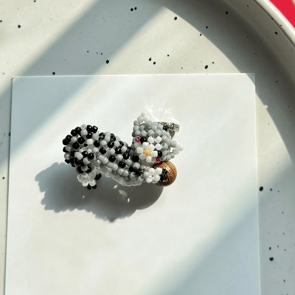 Beaded tabby cat charm on a white surface with a speckled background - verhalo handmade jewelry