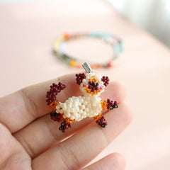 Hand holding a small beaded cat figure with a blurred colorful background