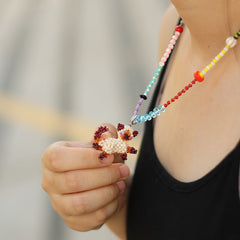 Close-up of a colorful beaded necklace with a hand holding it against a blurred background.
