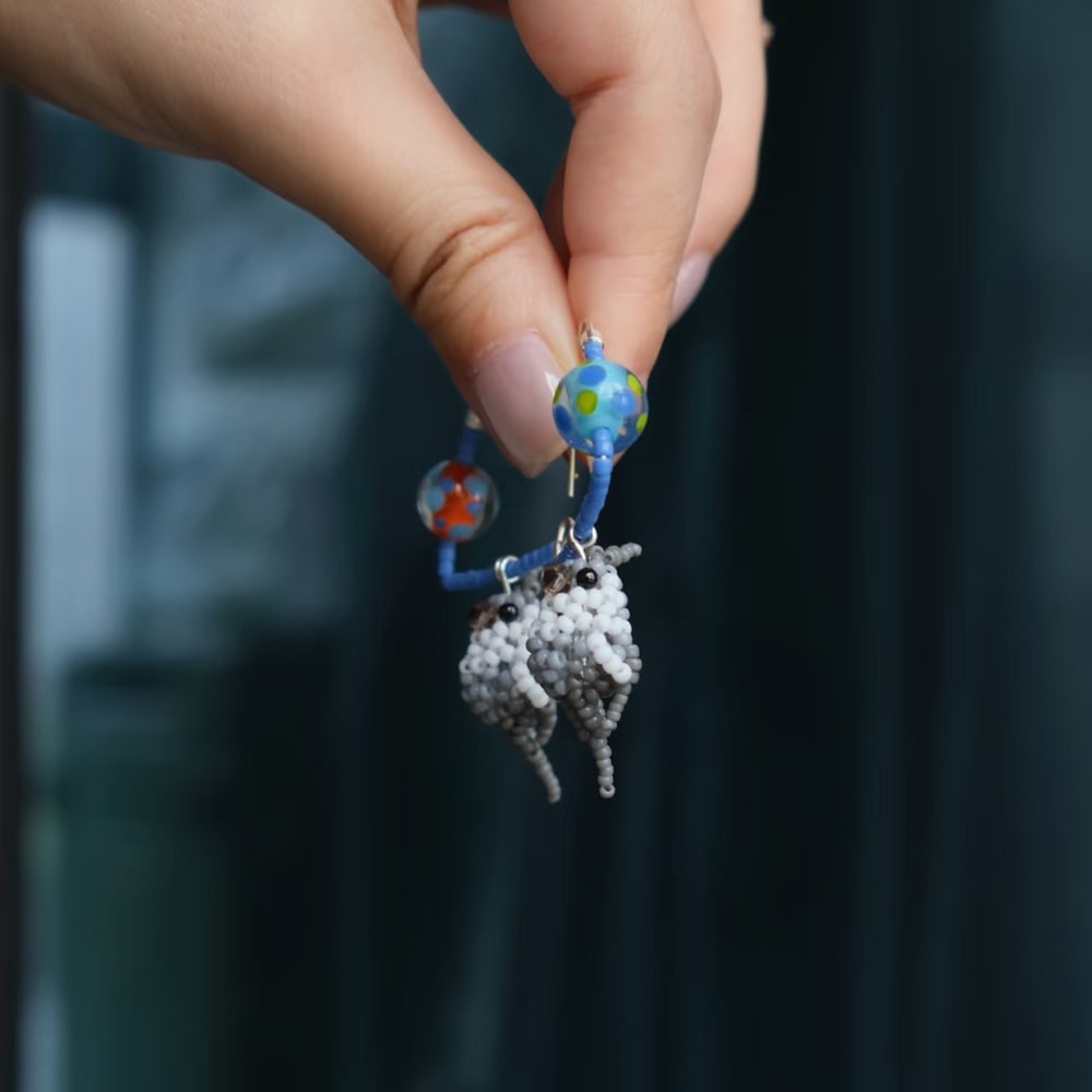 Hand holding a small, detailed parrot earrings against a blurred background