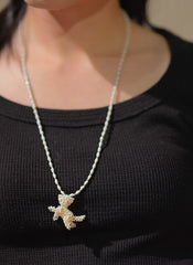Necklace with a white cat pendant worn by a person against a black background