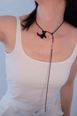 Person wearing a black beaded necklace with a cat pendant against a light background