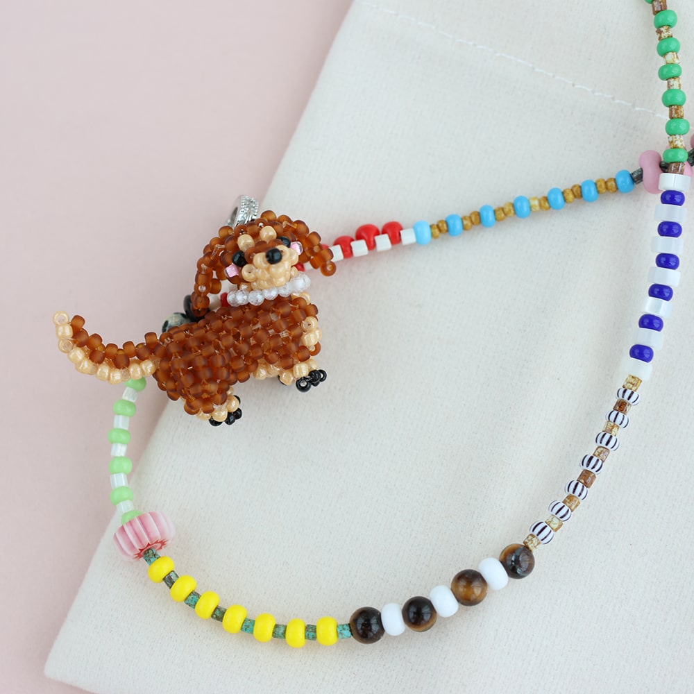 Beaded necklace with a DOG charm on a light pink background