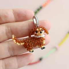 Beaded dog-shaped pendant held between fingers against a blurred background