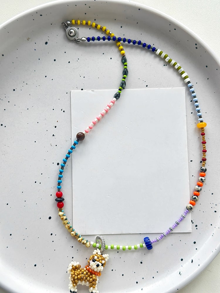 Colorful beaded shiba inu dog necklace with a small animal charm on a white speckled plate.