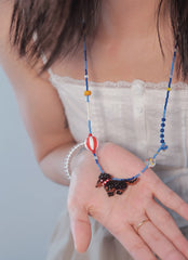 Person wearing a blue beaded necklace with a white top against a light background