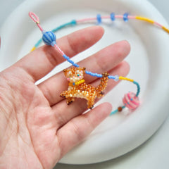 Hand holding a beaded cat charm on a white plate