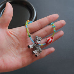 Hand holding a colorful beaded bracelet with a Schnauzer dog charm against a dark background