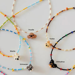 Colorful beaded necklaces with small dog figures labeled 'Poodle', 'Yorkie', 'Westie', and 'Schnauzer' on a light background.