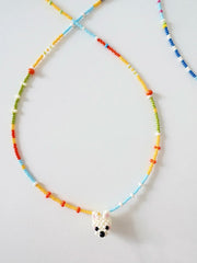 Colorful beaded necklace with a small white dog charm on a light gray background
