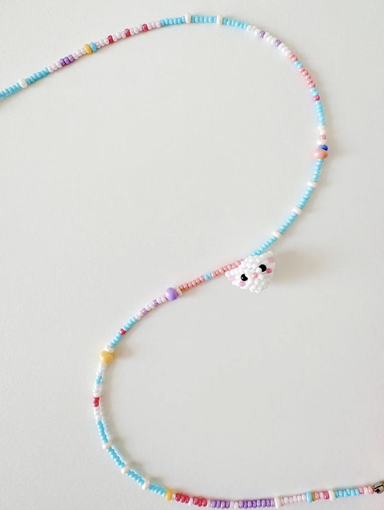 Colorful beaded necklace with a small white cat on a light gray background