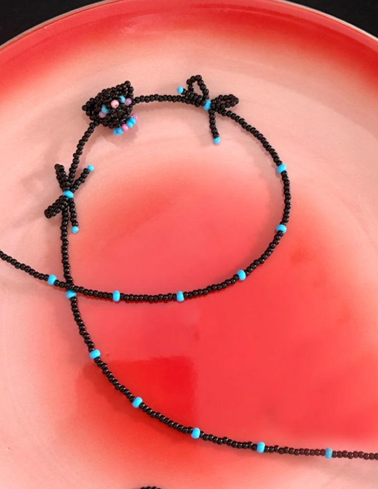 Black beaded necklace with blue beads on a red surface