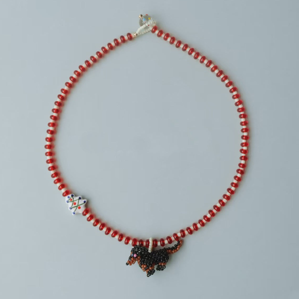 Handmade Necklace with red beads and a Dachshund  dog charm on a gray background - verhalo jewelry