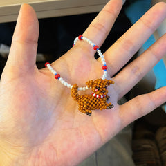 Hand wearing a beaded neckalce with a poodle dog charm against a blurred indoor background - verhalojewelry