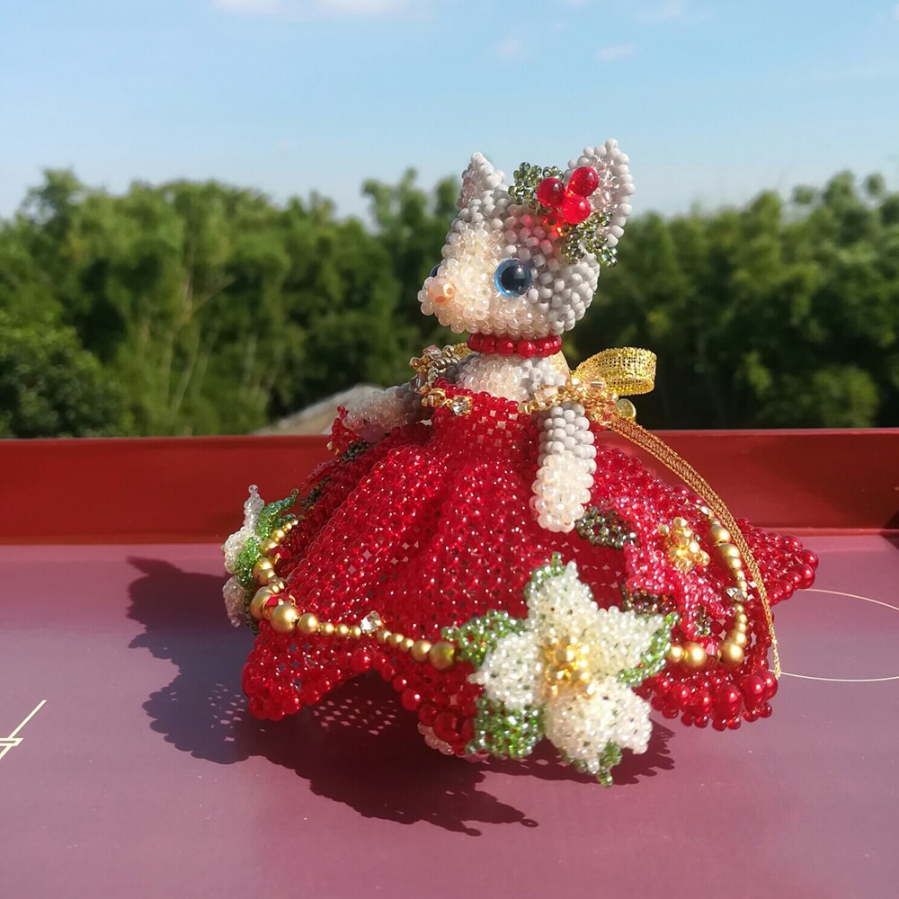 handmade beaded cat figurine with a red wedding dress on a red surface with a blurred green outdoor background