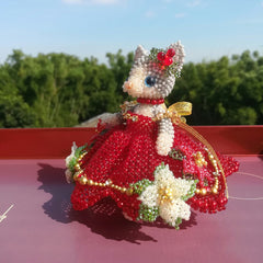 handmade beaded cat figurine with a red wedding dress on a red surface with a blurred green outdoor background