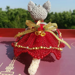 handmade beaded figurine with red wedding dress and  head on a pink surface with greenery in the background