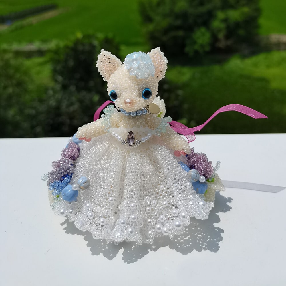 handmade cat figurine in a beaded white wedding dress with flowers on a white surface