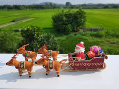 Knitted Santa Claus in a sleigh with reindeer against a green landscape.
