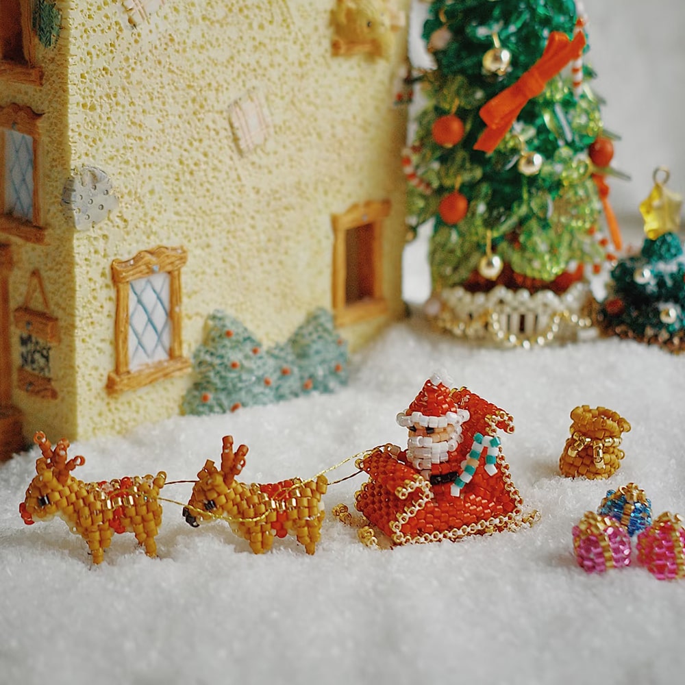 Miniature beaded Santa Claus with reindeer and sleigh in front of a decorated Christmas tree.