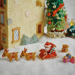 Miniature beaded Santa Claus with reindeer and sleigh in front of a decorated Christmas tree.